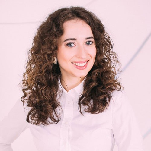 Image of Alumni student, Elena Tikhomirova, smiling in a white dress shirt and light background