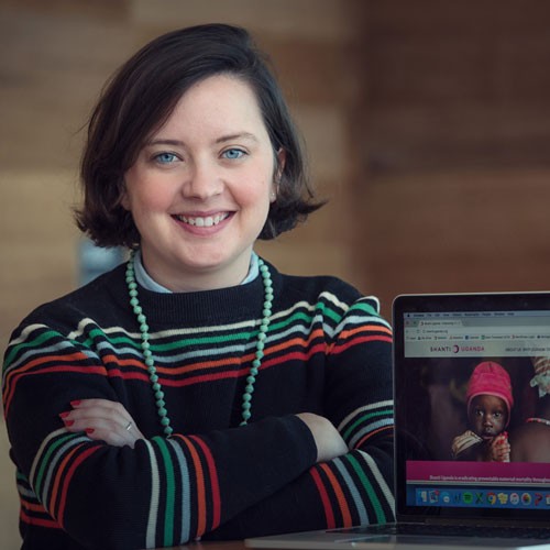 Image of Alumni student Kate Hyde sitting and leaning on a wooden table with a laptop in front of her