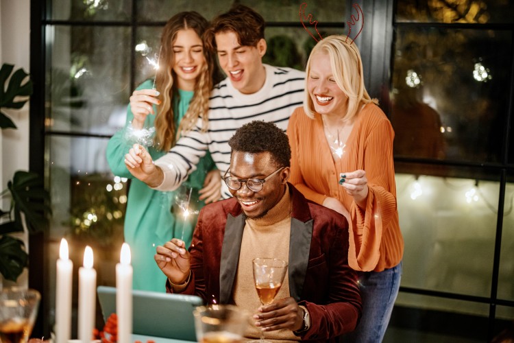 A group of 4 celebrating the new year around a laptop with sparklers and cocktails in hand