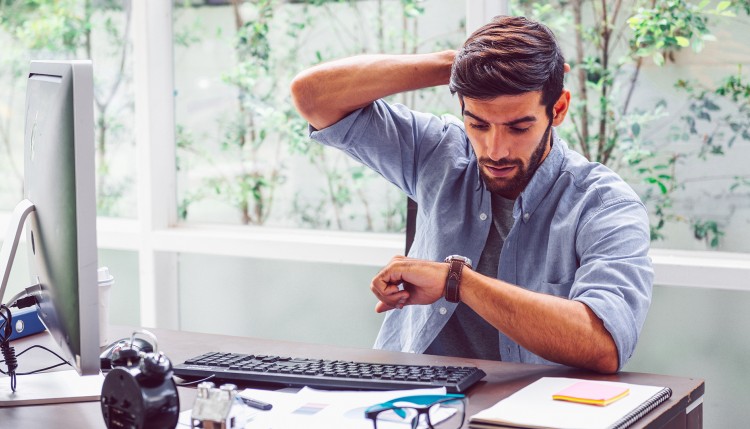 A businessman checking the time on his watch while sitting at a desk.